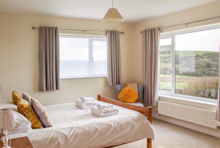 Cottage bedroom with double bed, windows and armchair with orange cushion