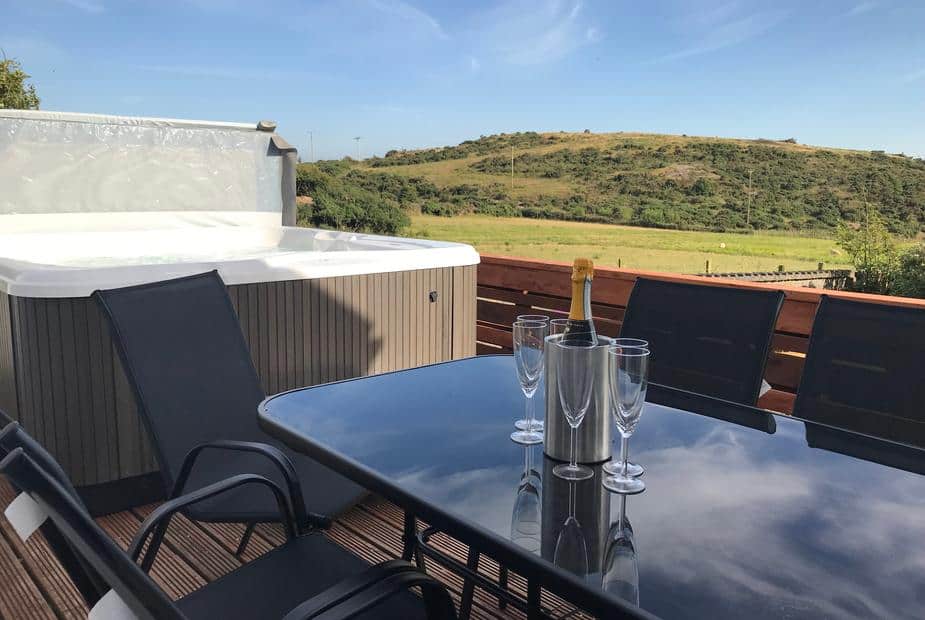Cottage deck with glass table, chairs and hot tub overlooking fields