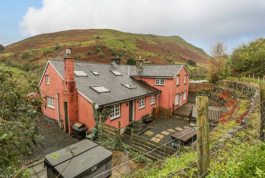 Cottage with slate roof and patio, set against hillside with stone wall fencing