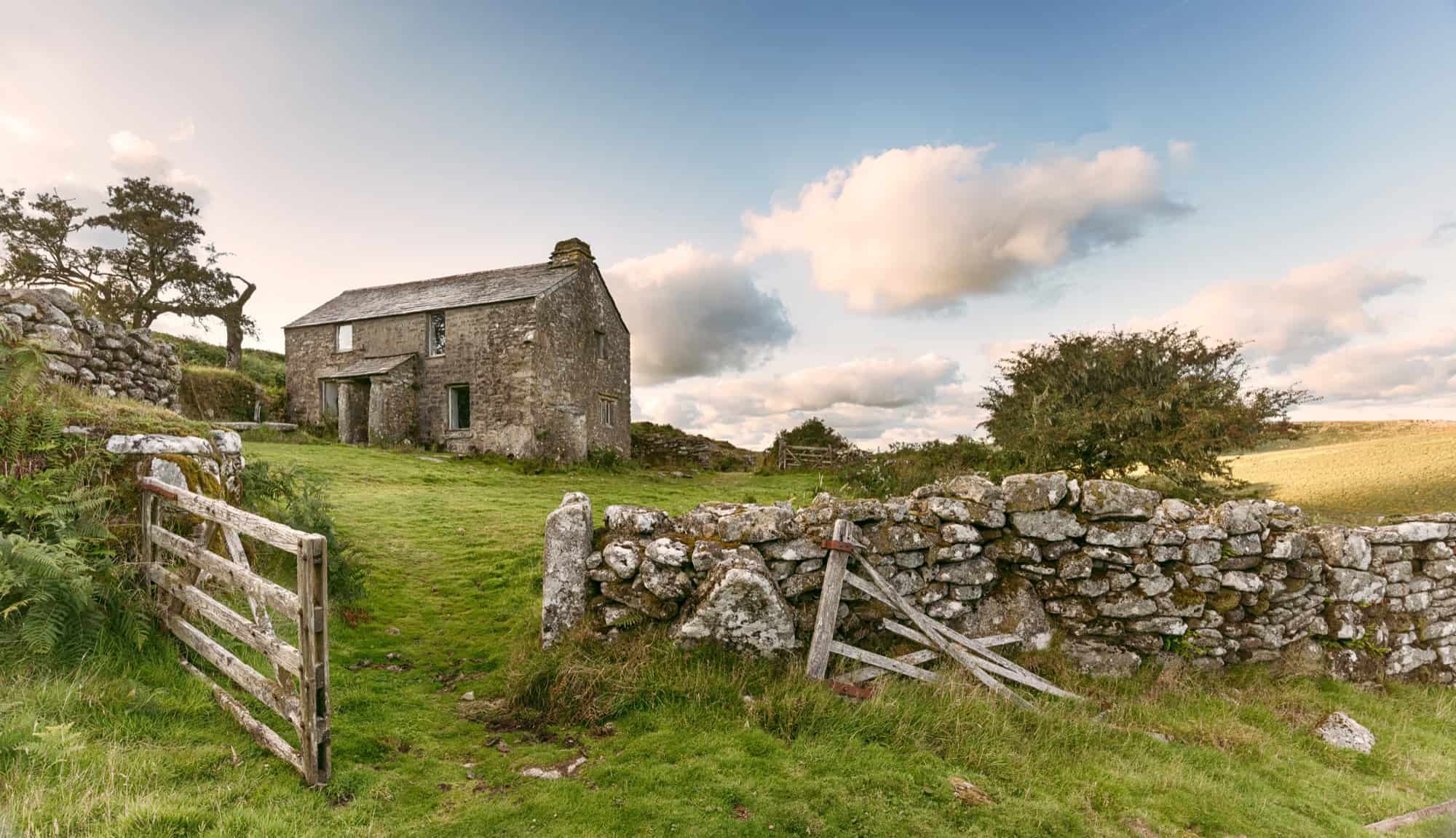 A remote stone farmhouse with a dry-stone wall set in the rugged, open moorlands of the North of England.