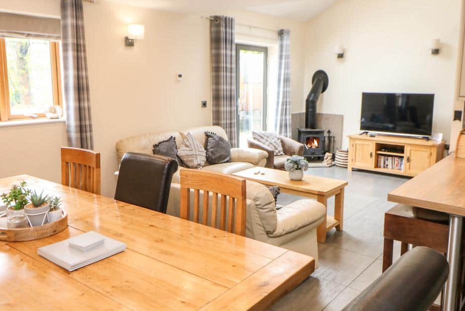 Cottage living room with wood burner, sofa, TV and dining table in foreground