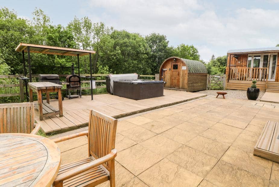 Patio at cottage with hot tub, outdoor seating, barbecue and wooden sauna hut