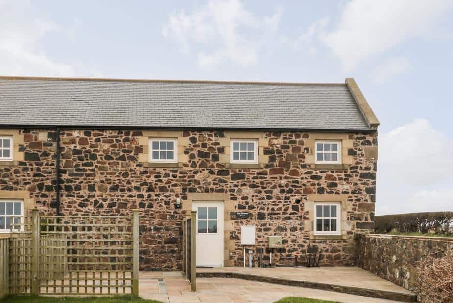 Stone exterior of High Hemmel House with fenced patio and hedgerow.
