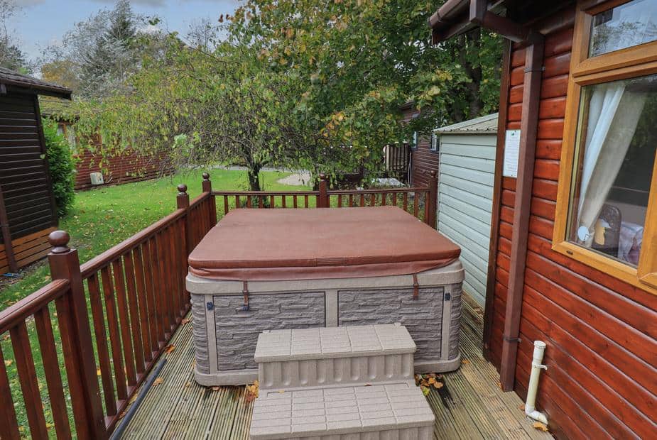 Lodge decking with covered hot tub and steps next to wooden exterior wall