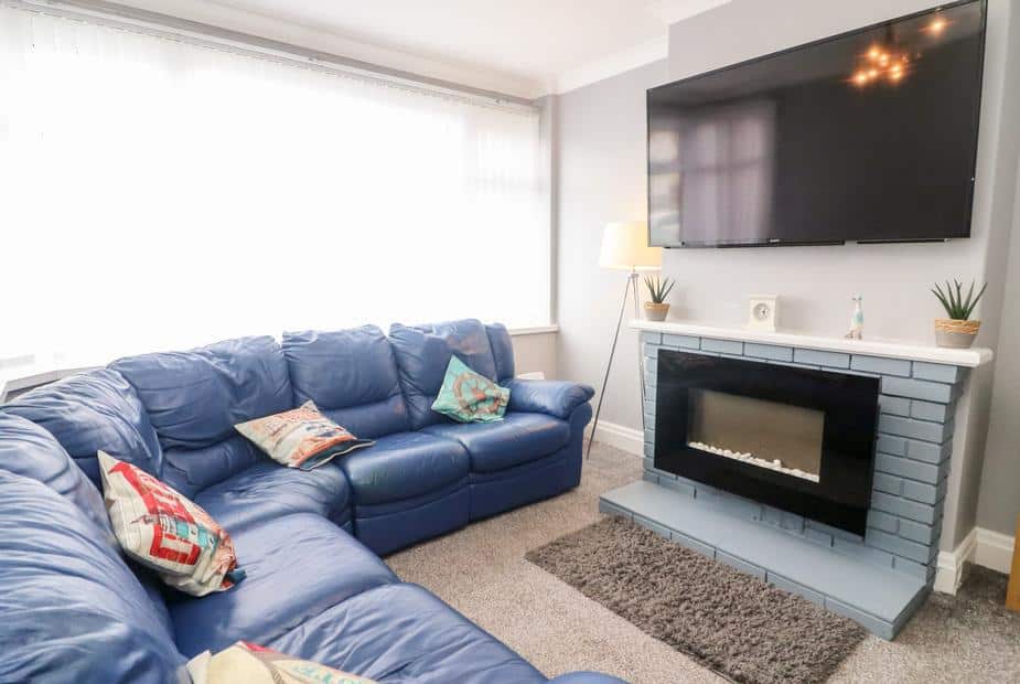 Cottage living room with blue corner sofa and wall-mounted television above fireplace