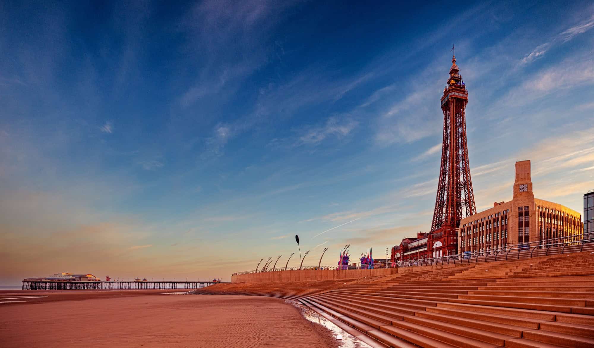 Sunrise over Blackpool promenade featuring the iconic Tower and empty steps leading to the beach, capturing a peaceful morning atmosphere.