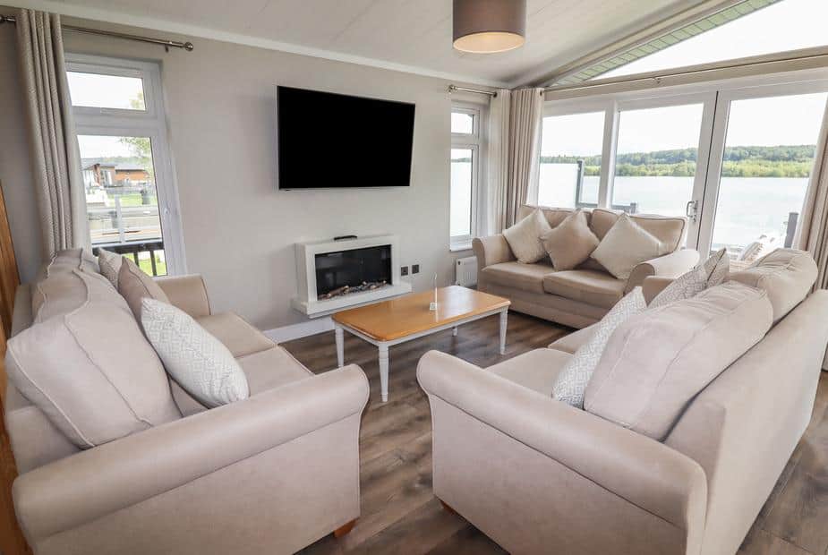 Living room with sofas, wall-mounted TV, fireplace and lake view through windows