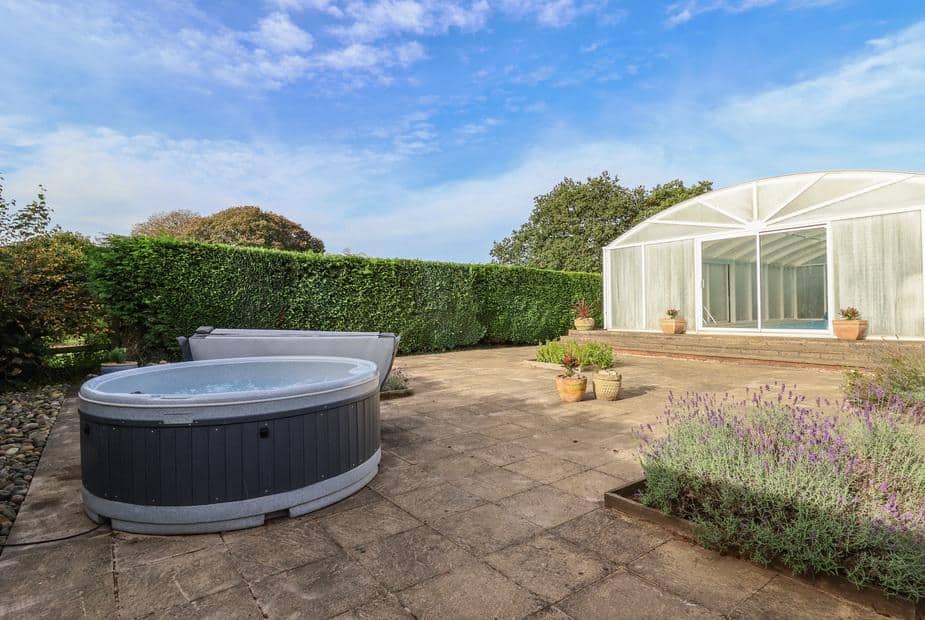 Patio at lodge with hot tub and potted plants near hedge and glazed outbuilding