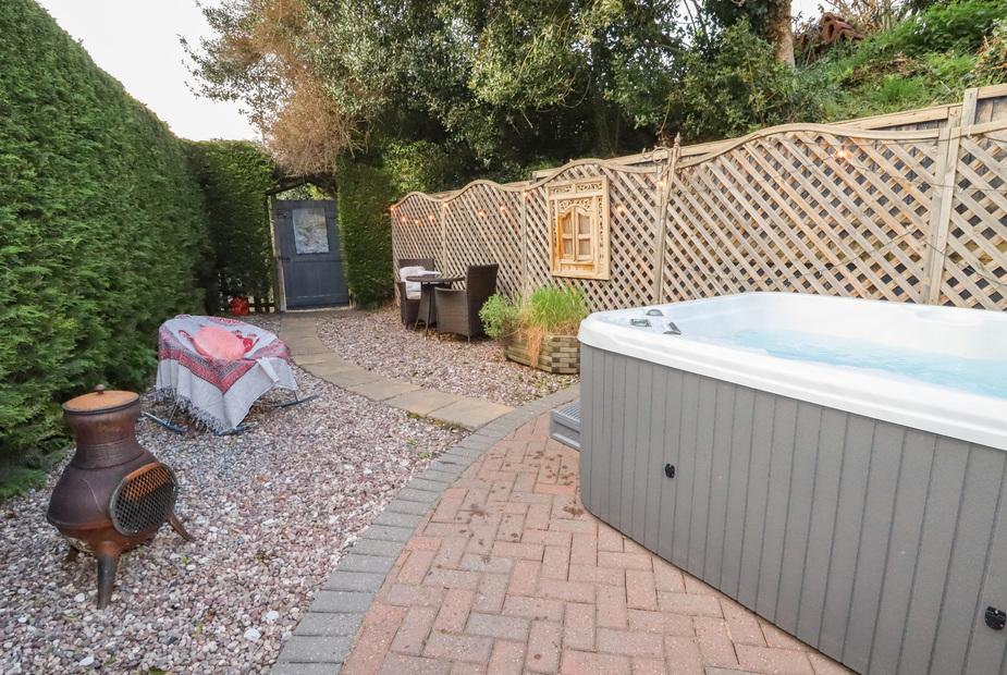 Cottage garden with hot tub, patio table and chairs, chiminea, and trellis fencing