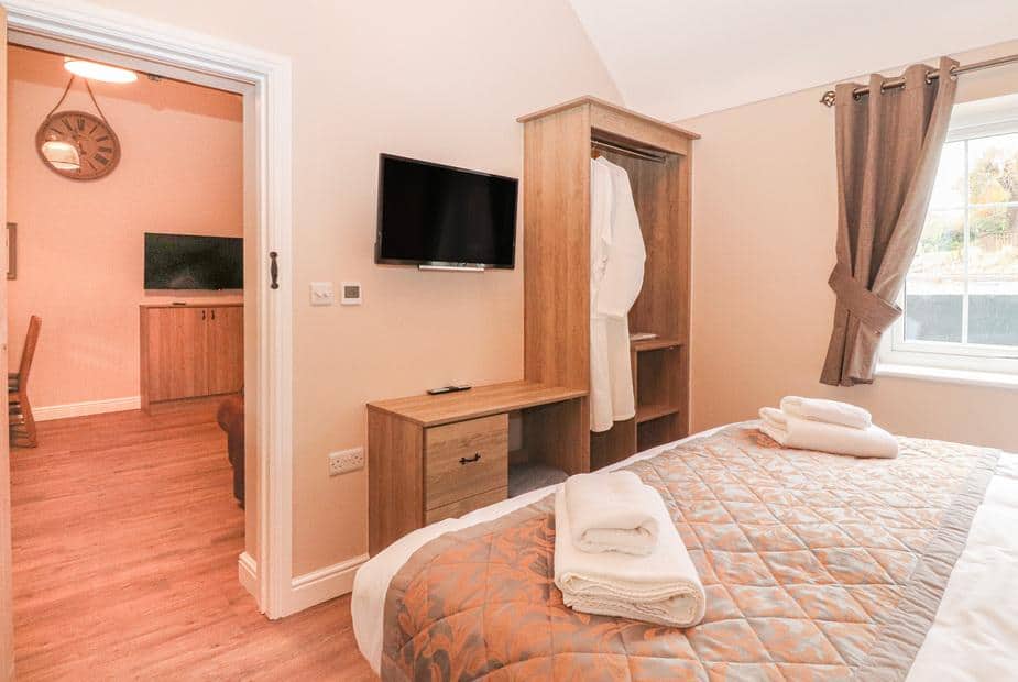 Cottage bedroom with double bed, TV, wardrobe and window with curtains