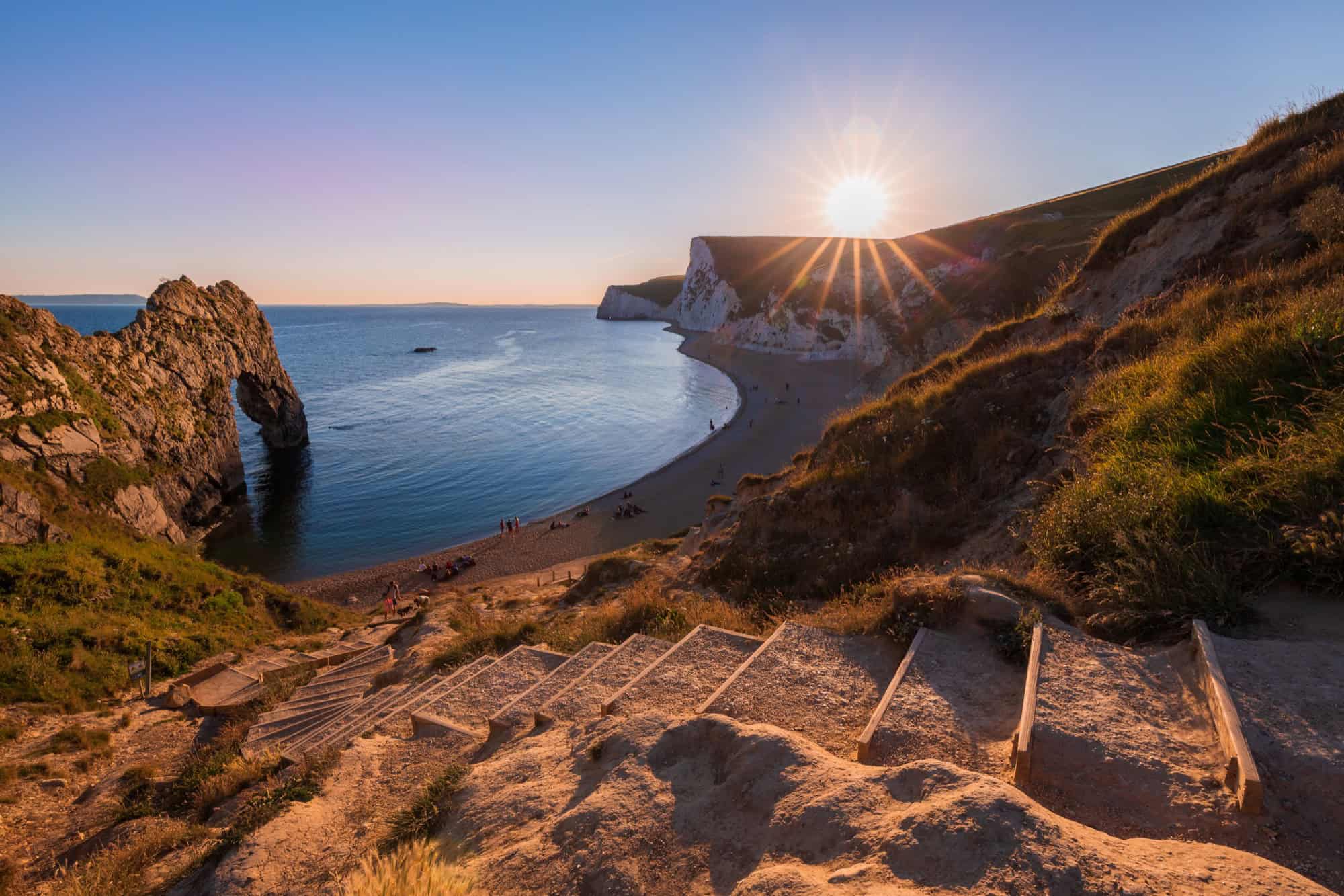 Steps leading down the cliff to Durdle Door on the Jurassic Coast, bathed in warm golden sunset light.