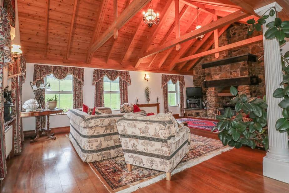 Cottage lounge with exposed wooden beams, stone fireplace, and patterned sofas