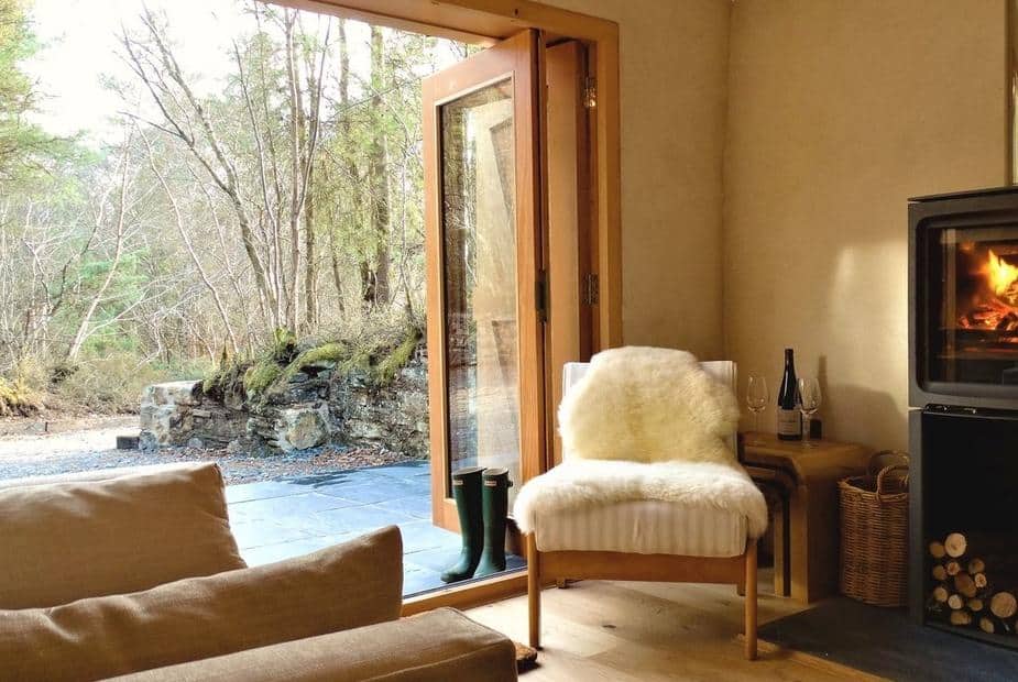 Cottage lounge with chair, wood burner, and open doors to patio and woodland