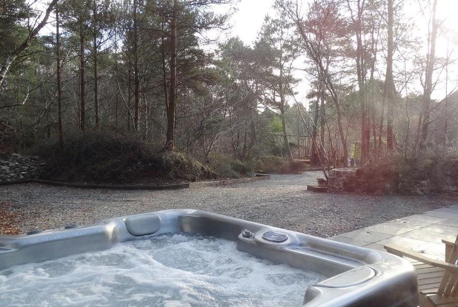 Hot tub on stone patio outside cottage with woodland views
