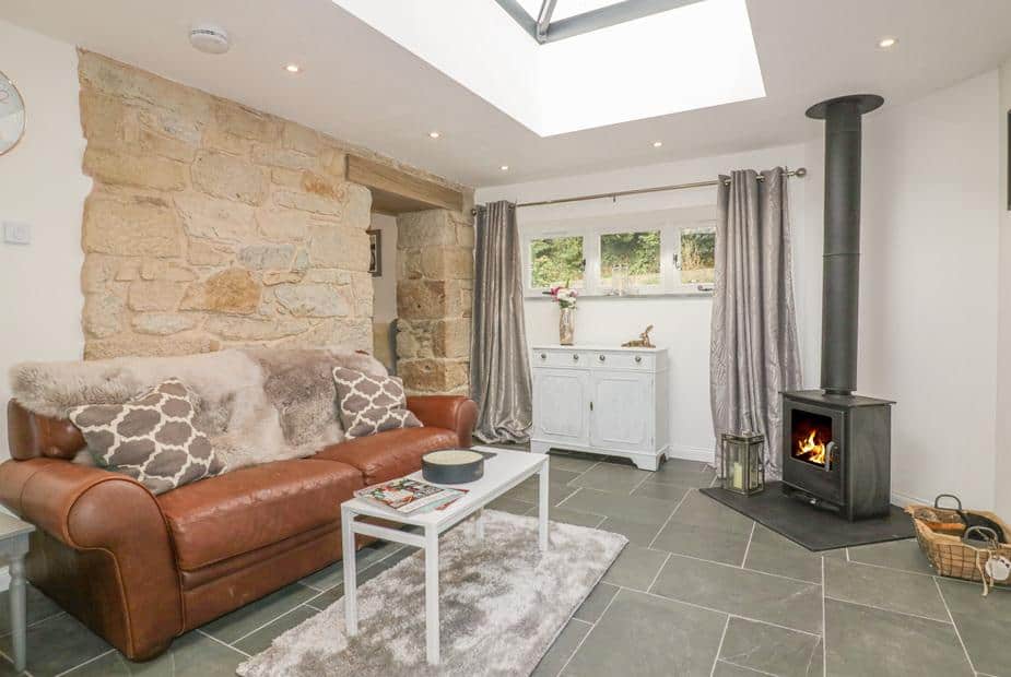 Cottage lounge with leather sofa, stone wall and wood-burning stove