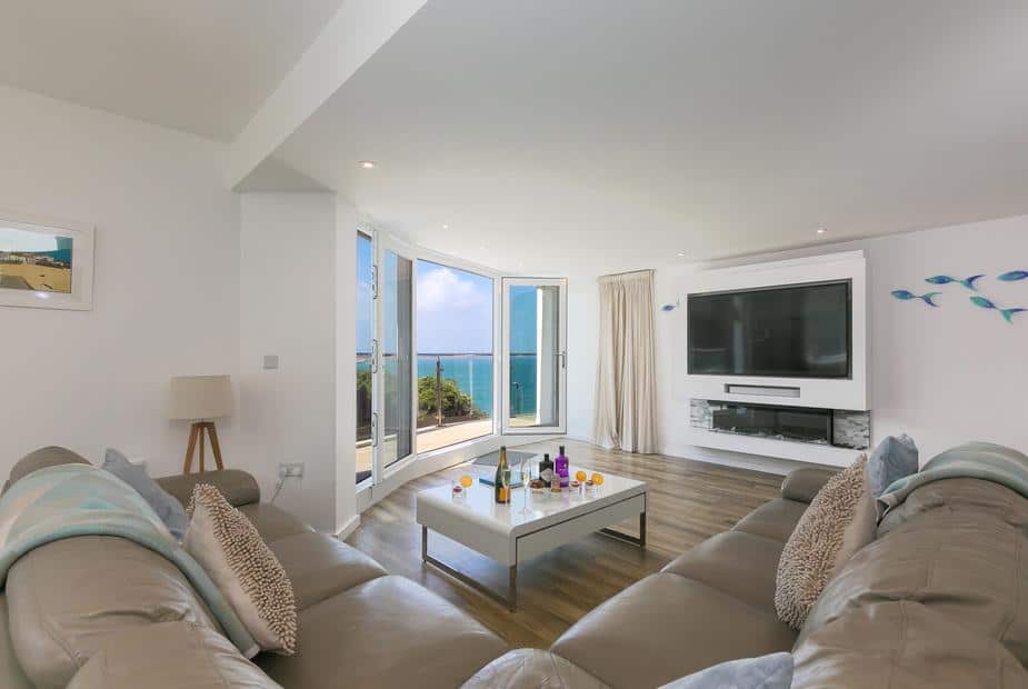 Cottage living room with corner sofas, large TV and sea view through open doors