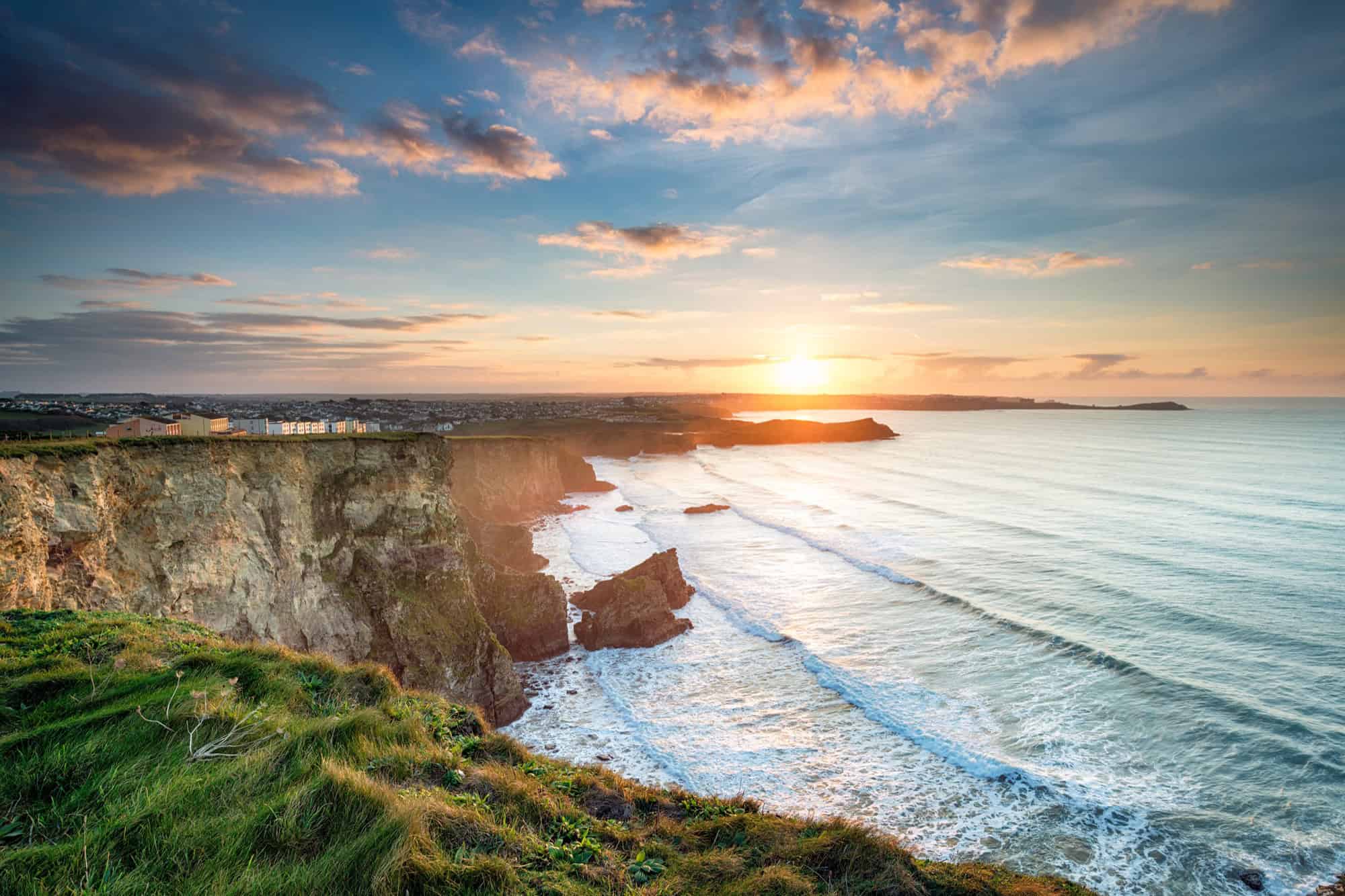 Dramatic sunset over Porth Beach in Newquay, featuring rugged cliffs, rolling Atlantic waves, and a colourful evening sky.