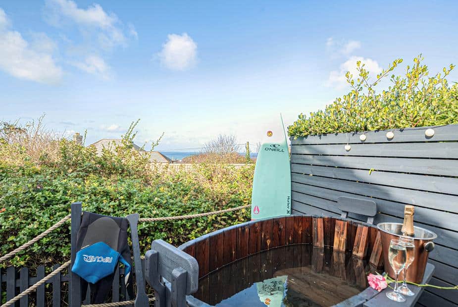 Cottage garden hot tub with surfboard and champagne, partial sea view in background