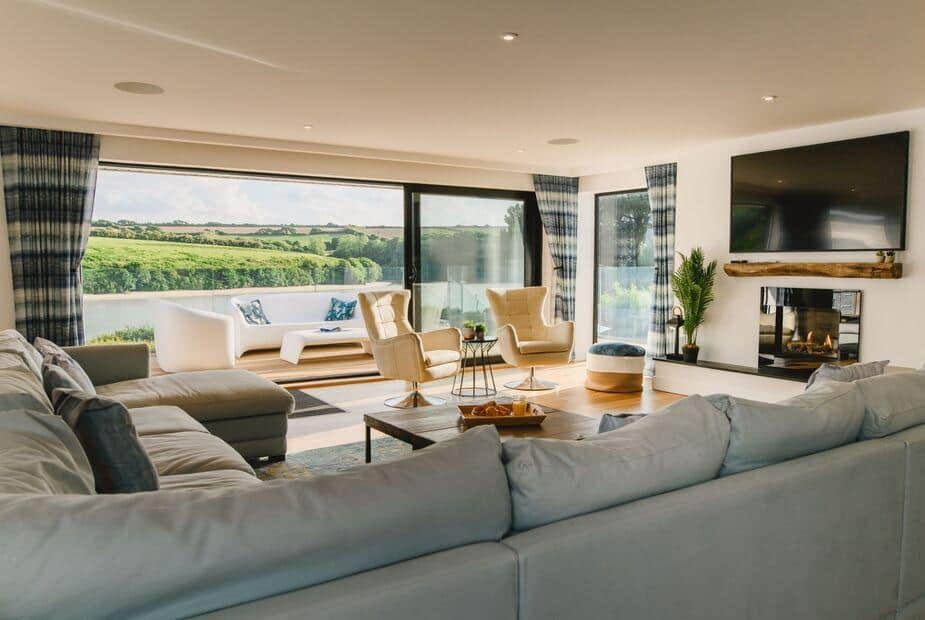 Cottage lounge with corner sofa, fireplace and large windows overlooking countryside