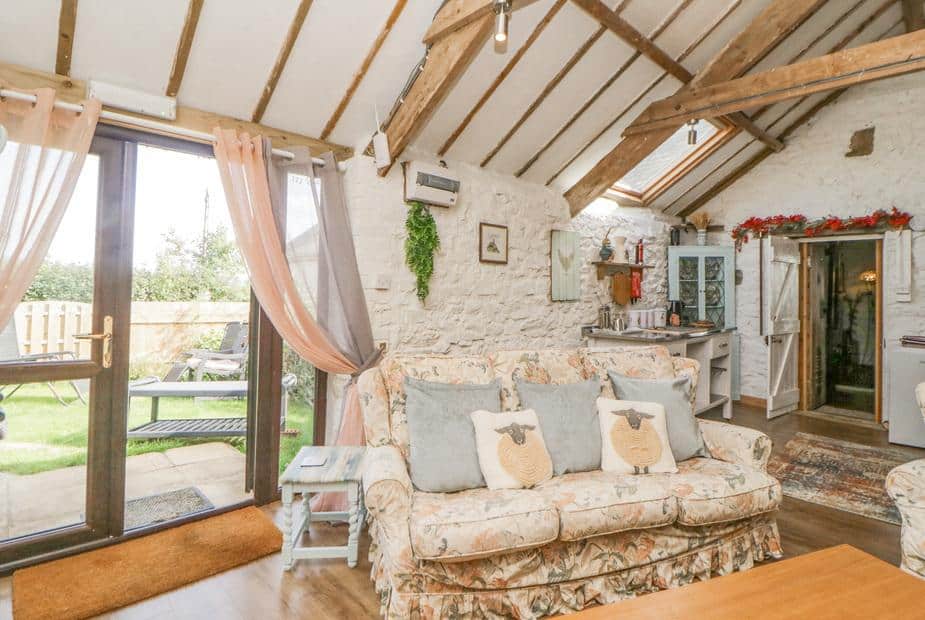 Cottage lounge with floral sofa and exposed beams, doors opening to garden