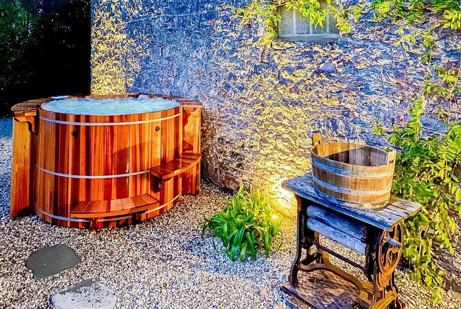 Cottage courtyard with wooden hot tub and vintage washing mangle on gravel.