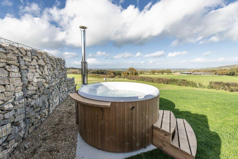 Lodge garden with round wooden hot tub and stone wall, overlooking countryside