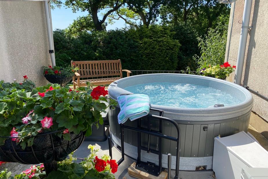 Cottage patio with round hot tub, wooden bench and potted flowers