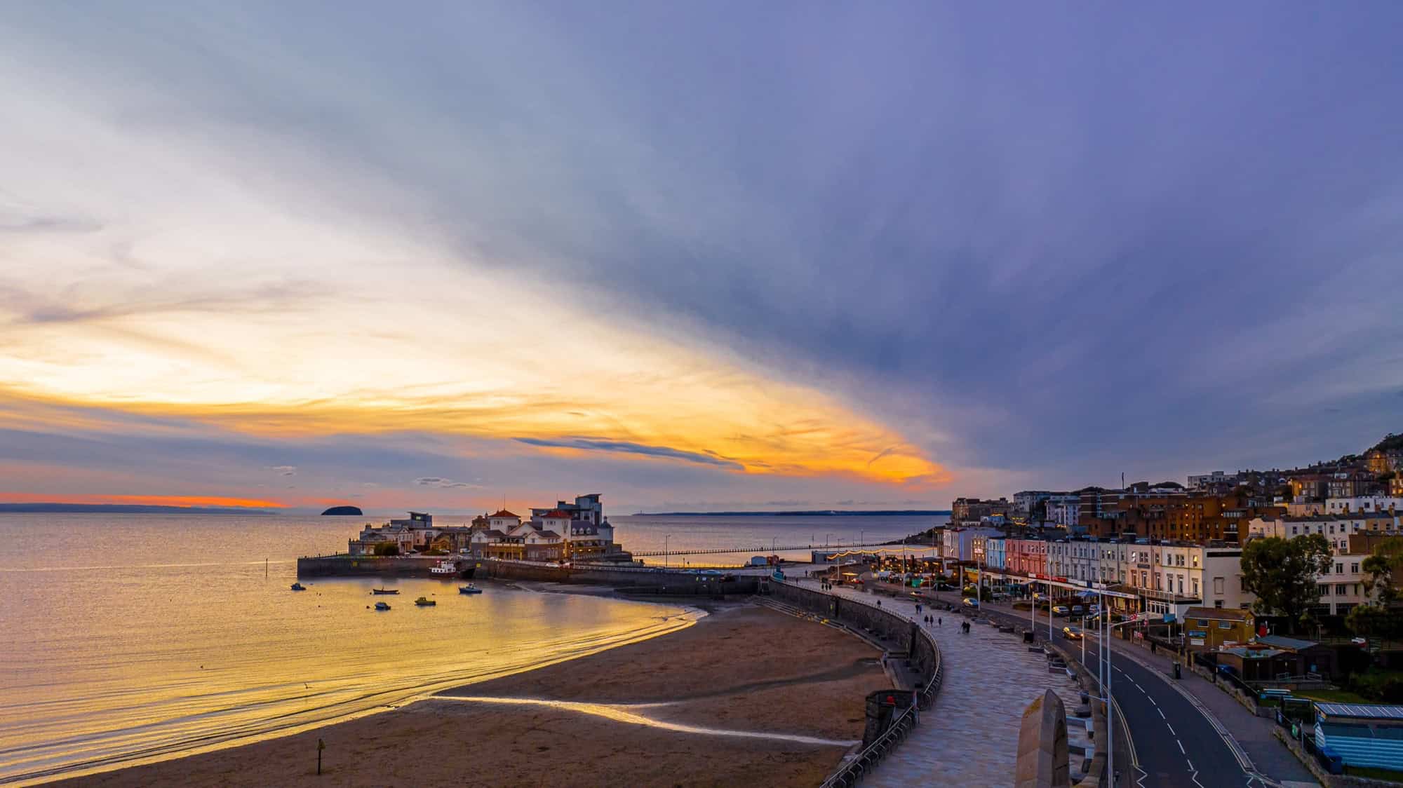 Aerial view of Weston-super-Mare at sunset, showing the sweeping sandy beach, the town seafront, and a dramatic golden horizon.