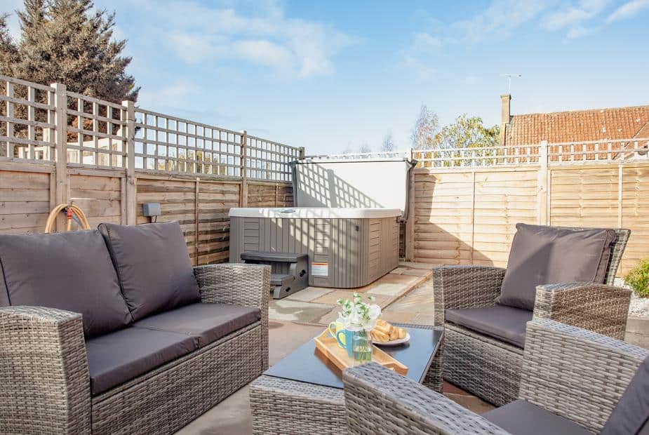 Patio with rattan seating and hot tub in fenced cottage garden