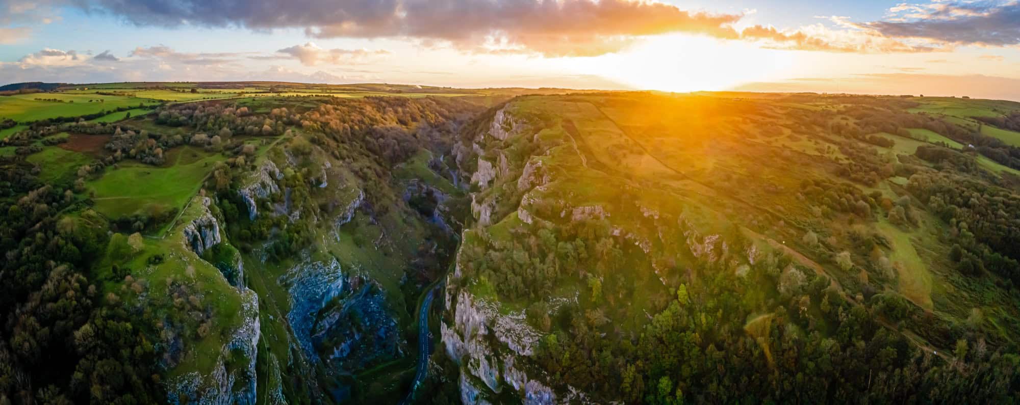 Aerial view of Cheddar Gorge at sunset, with golden light illuminating the dramatic limestone cliffs and the rolling Mendip Hills.