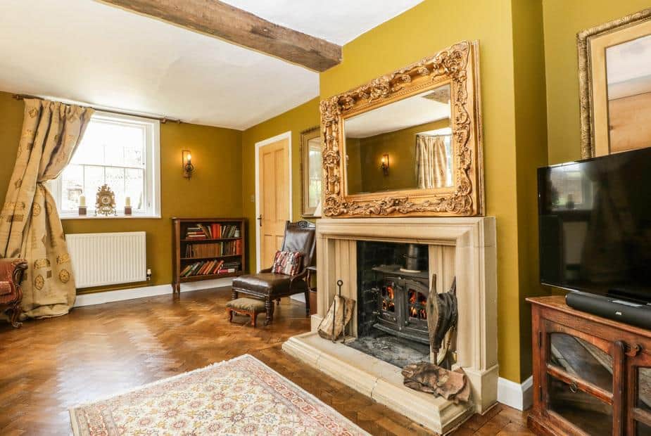 Cottage lounge with wood-burning stove, ornate mirror and exposed ceiling beam