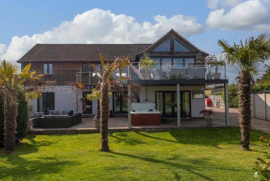 Longmynd cottage exterior with balcony, palm trees and outdoor hot tub on patio.