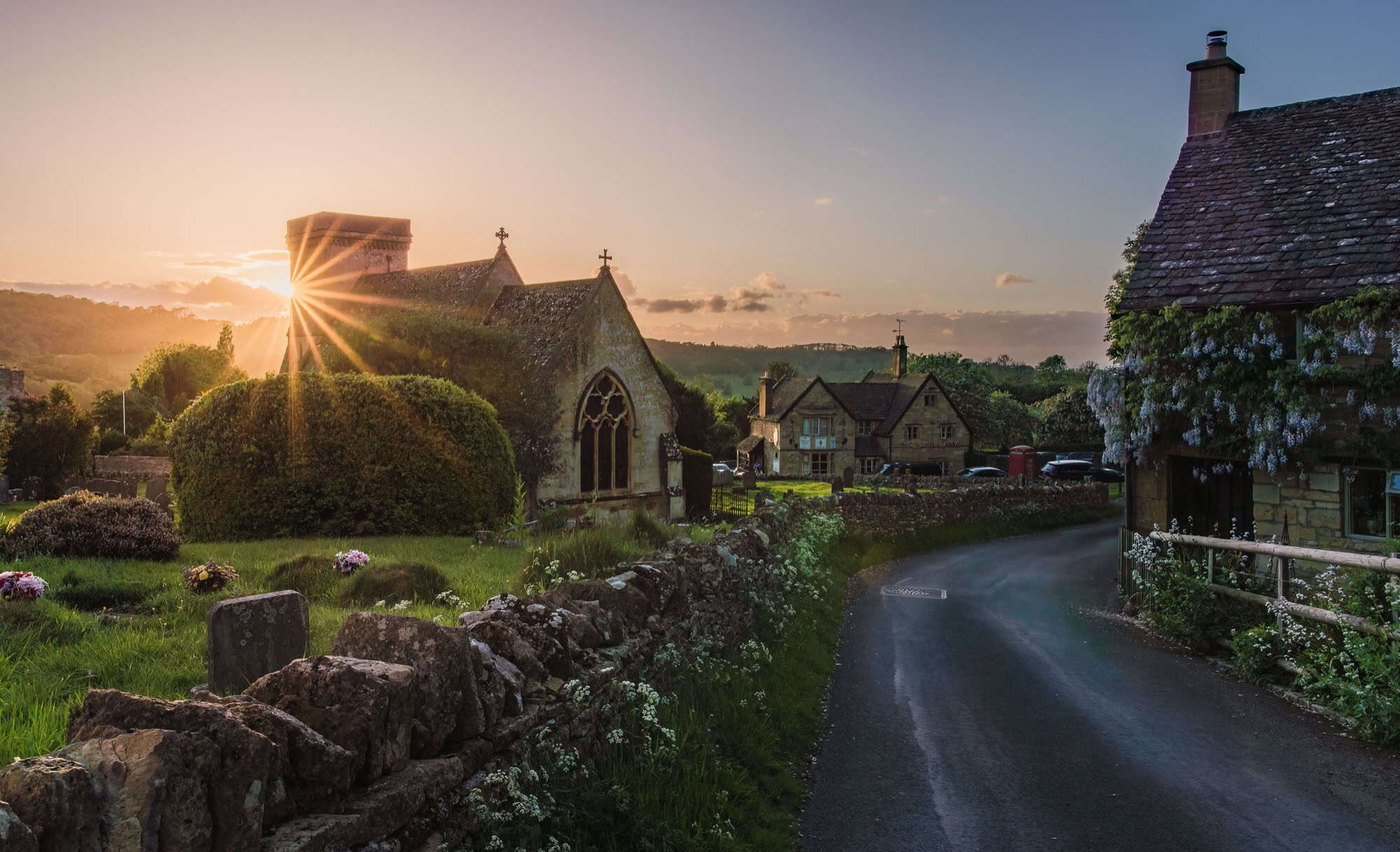 Golden sunburst shining over the historic stone church and cottages of Snowshill village in the Cotswolds.