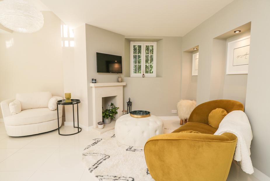 Cottage lounge with mustard armchair, round ottoman and wall-mounted TV above fireplace
