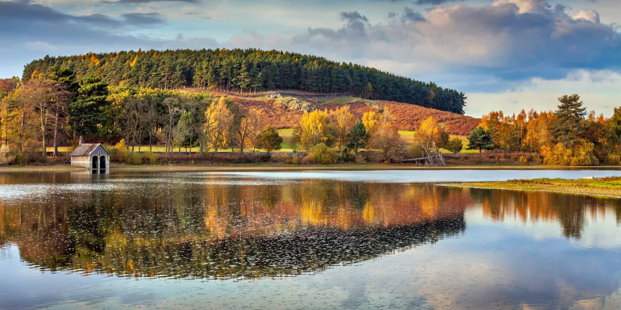 Autumn colours and a stone boathouse reflecting in the calm waters of Cropston Reservoir in Leicestershire.