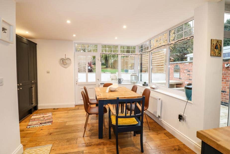 Cottage dining area with wooden table and chairs by large windows and patio door