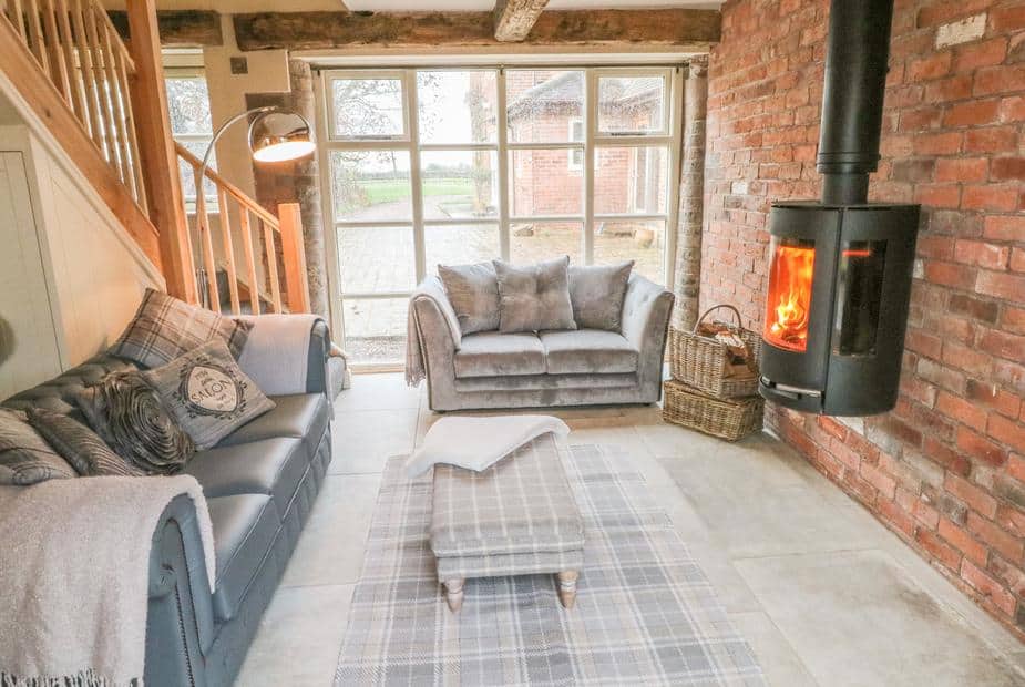 Cottage lounge with log burner, two sofas, footstool and exposed brick wall