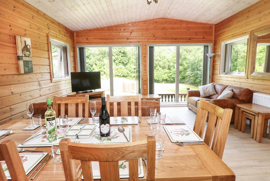 Lodge dining area with wooden table, TV, sofa and sliding glass doors to garden