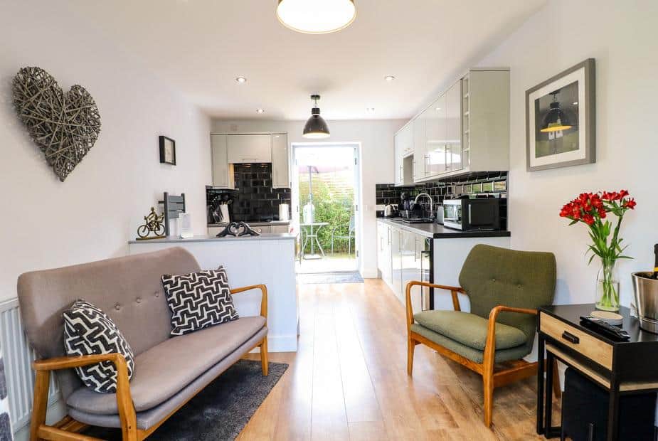 Cottage living area with sofa, armchair and modern kitchen leading to patio garden