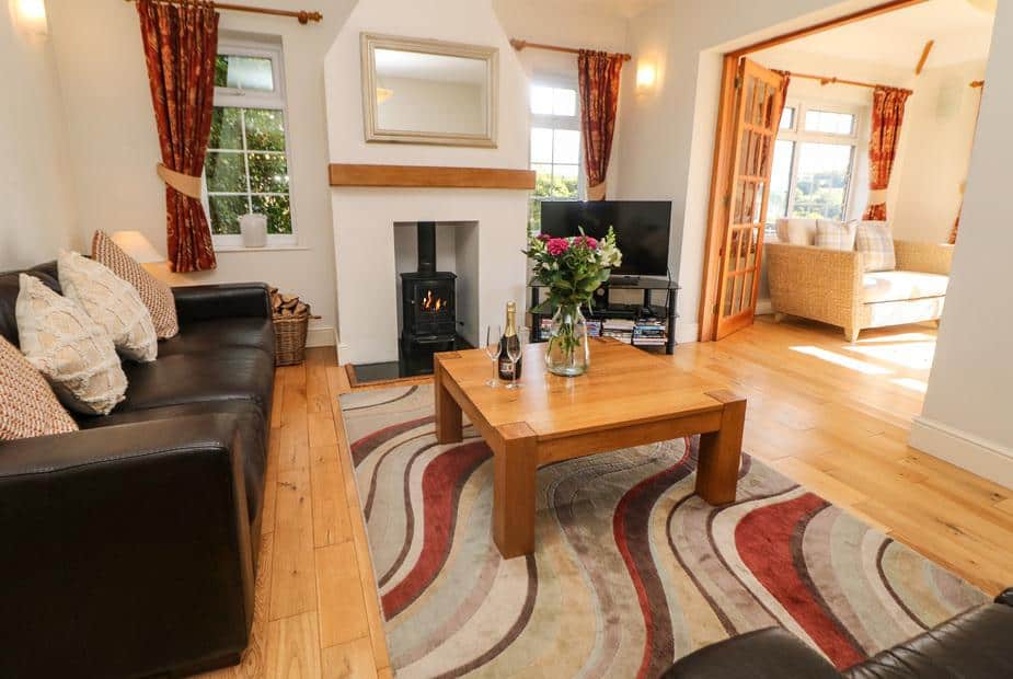 Cottage lounge with wood burner, leather sofa, and coffee table on patterned rug