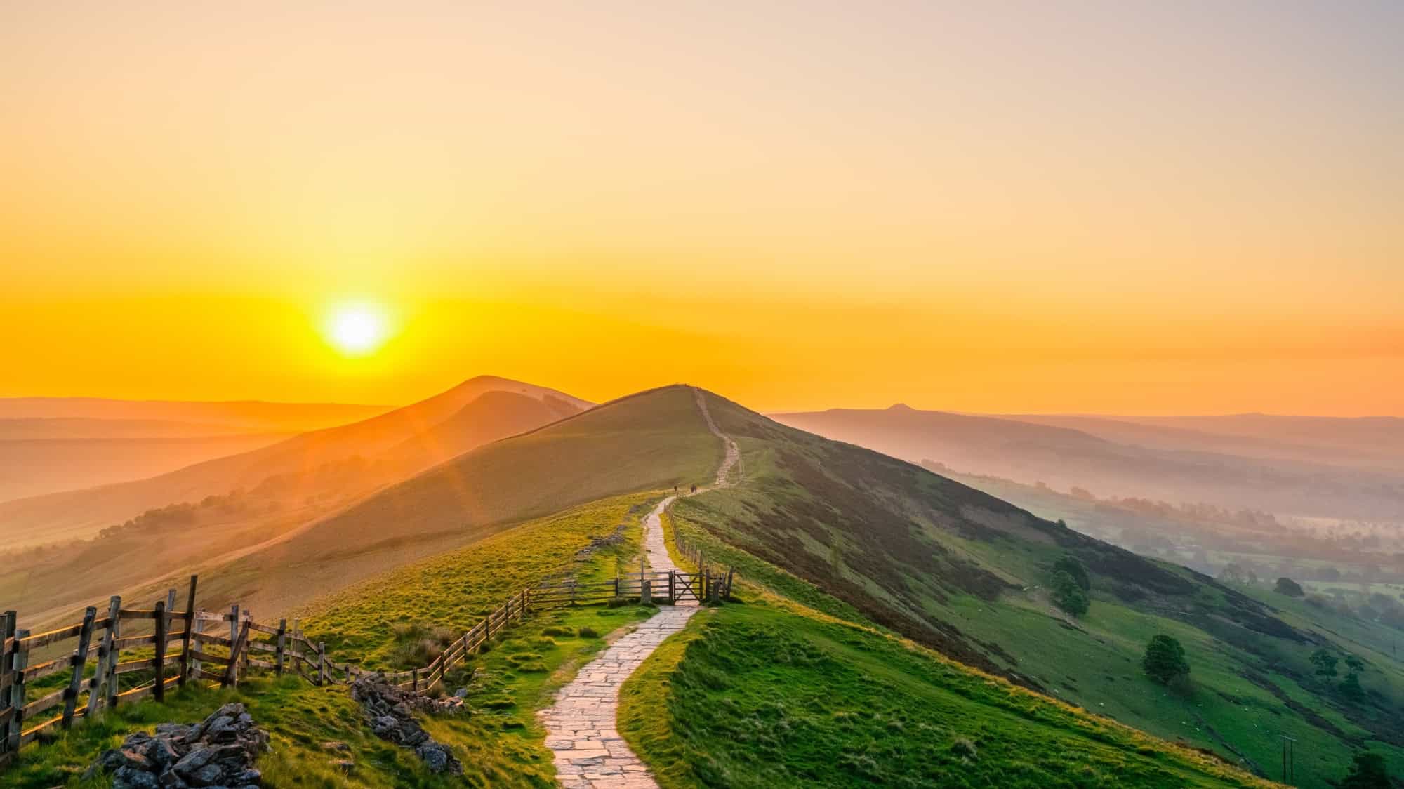 Golden sunrise sunburst shining over the stone path leading up to the summit of Mam Tor in the Peak District.