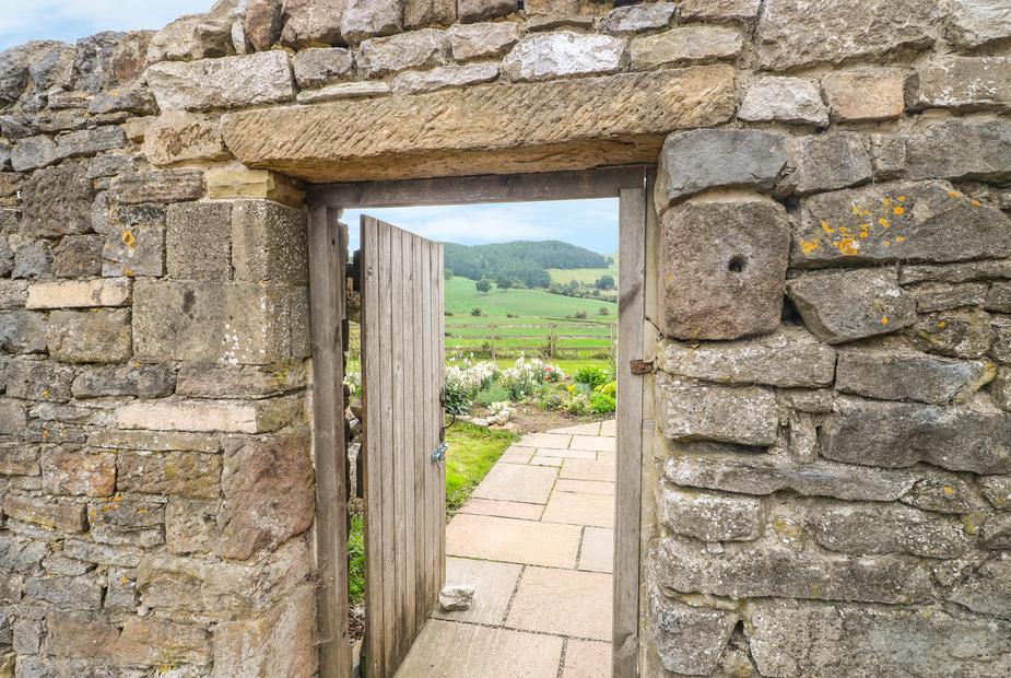Cottage stone wall with wooden gate opening to garden and countryside view