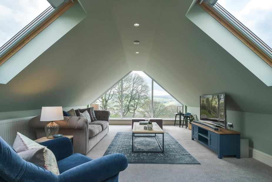 Cottage loft living room with sofas, TV unit and large triangular window