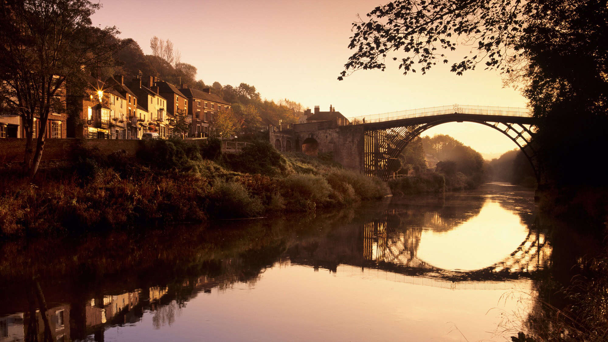 Golden sunset light illuminating the historic Iron Bridge crossing the River Severn in Shropshire, Midlands.