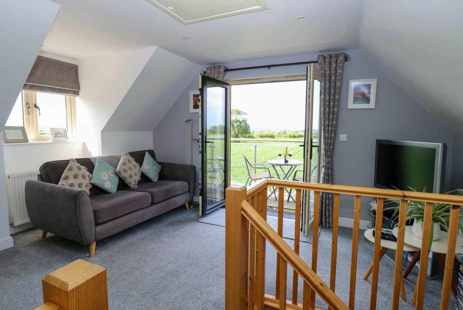 Cottage lounge with sofa, TV and patio doors opening to balcony with table and chairs