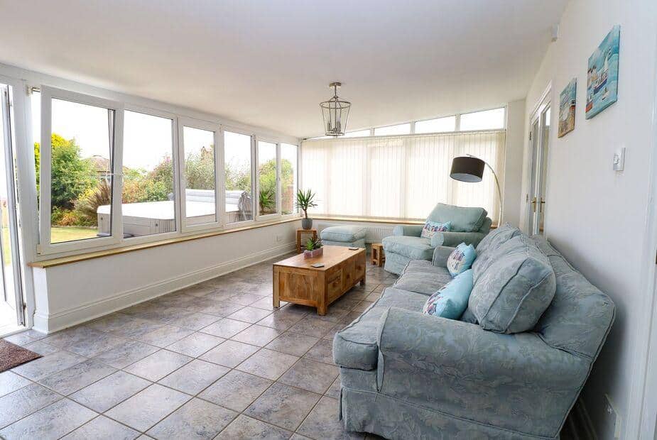 Cottage sunroom with large windows, tiled floor and two sofas around a wooden coffee table