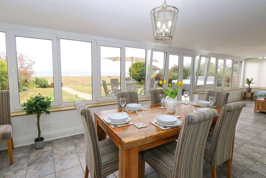 Cottage dining area with set table and large windows overlooking garden and patio