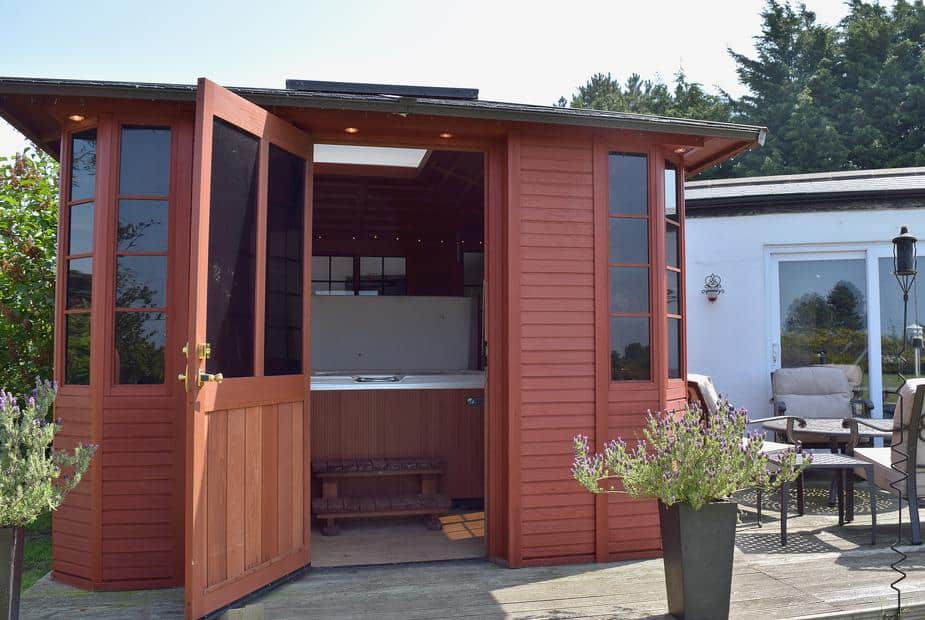 Lodge cabin with open wooden doors revealing indoor hot tub on decking area