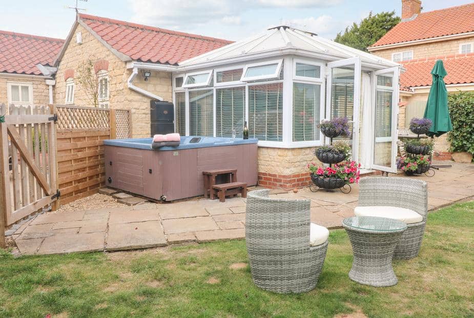 Cottage patio with hot tub, rattan chairs and glass-topped table in garden area