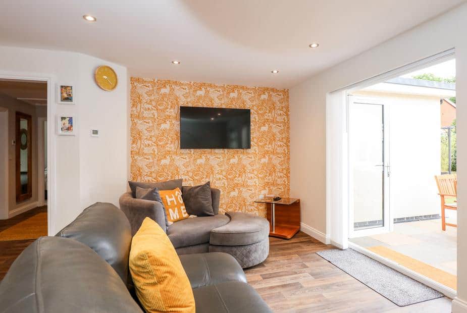 Cottage lounge with wall-mounted TV, round chair and patio doors to outside seating area
